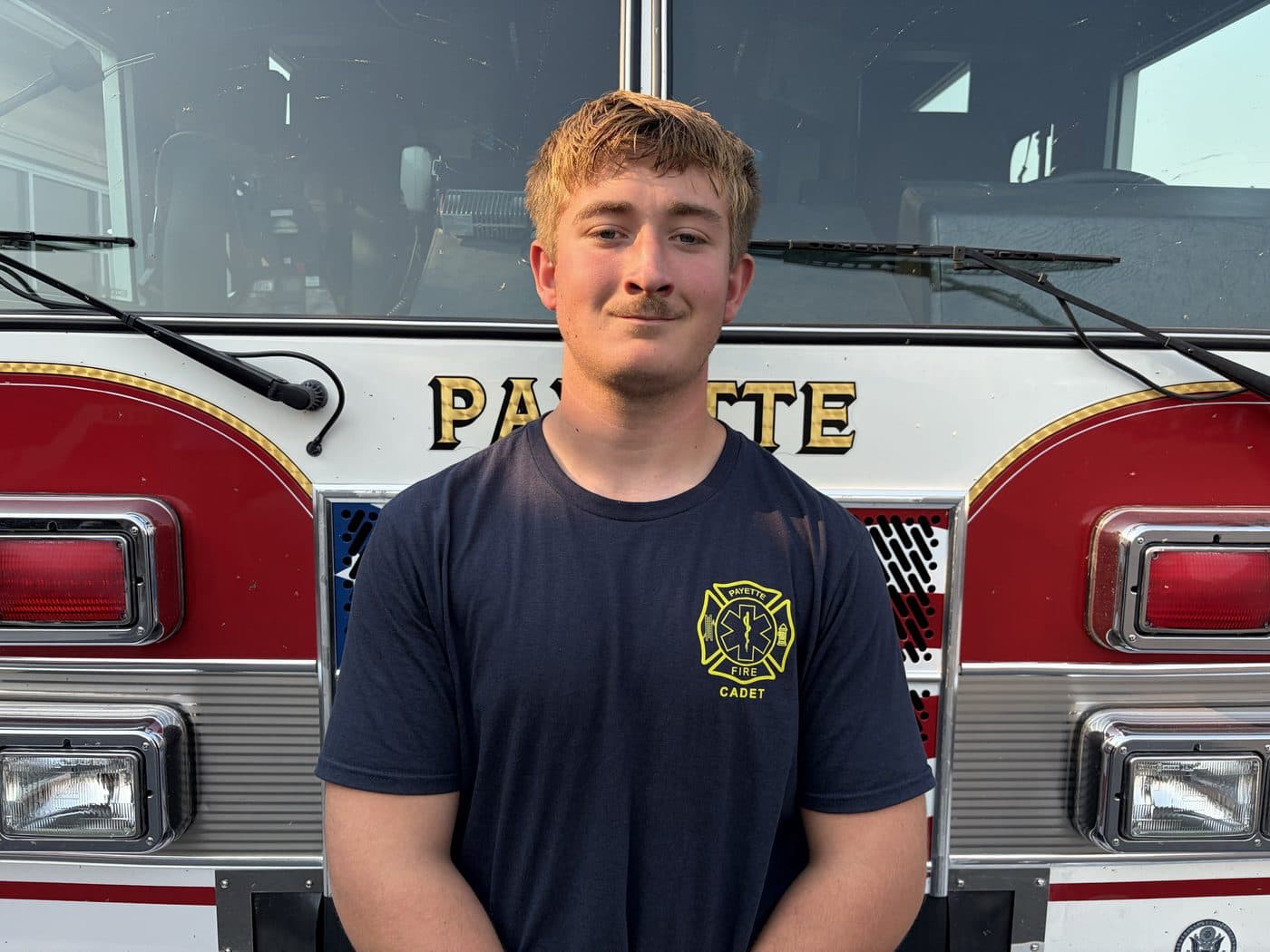 Cadet Firefighter Grady Coen in a Payette Fire cadet shirt, standing in front of a fire engine.