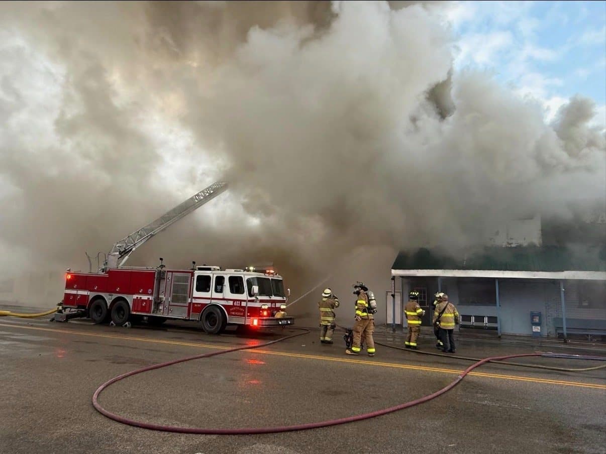 Ladder 611 with its aerial raised at a working structure fire, crews on the street with hose lines and heavy smoke overhead